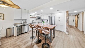 A modern kitchen with white cabinets, stainless steel appliances, and a wooden dining table with bar stools.