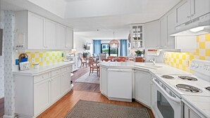 A modern kitchen with white cabinetry, a central island, and a stove. - Ground floor 2/2 condo with a large patio, just steps from the pool and beach access (New Smyrna Beach)