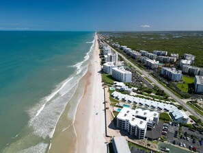 An aerial view of a coastal residential area with beachfront properties, including multi-story buildings and a beach. - Ground floor 2/2 condo with a large patio, just steps from the pool and beach access (New Smyrna Beach)