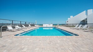 A rectangular swimming pool with clear blue water, surrounded by a tiled deck with white lounge chairs. - Ground floor 2/2 condo with a large patio, just steps from the pool and beach access (New Smyrna Beach)
