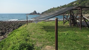 Una zona costera con una estructura de madera, posiblemente un mirador o una pequeña pérgola, con vista a una playa rocosa y al mar.