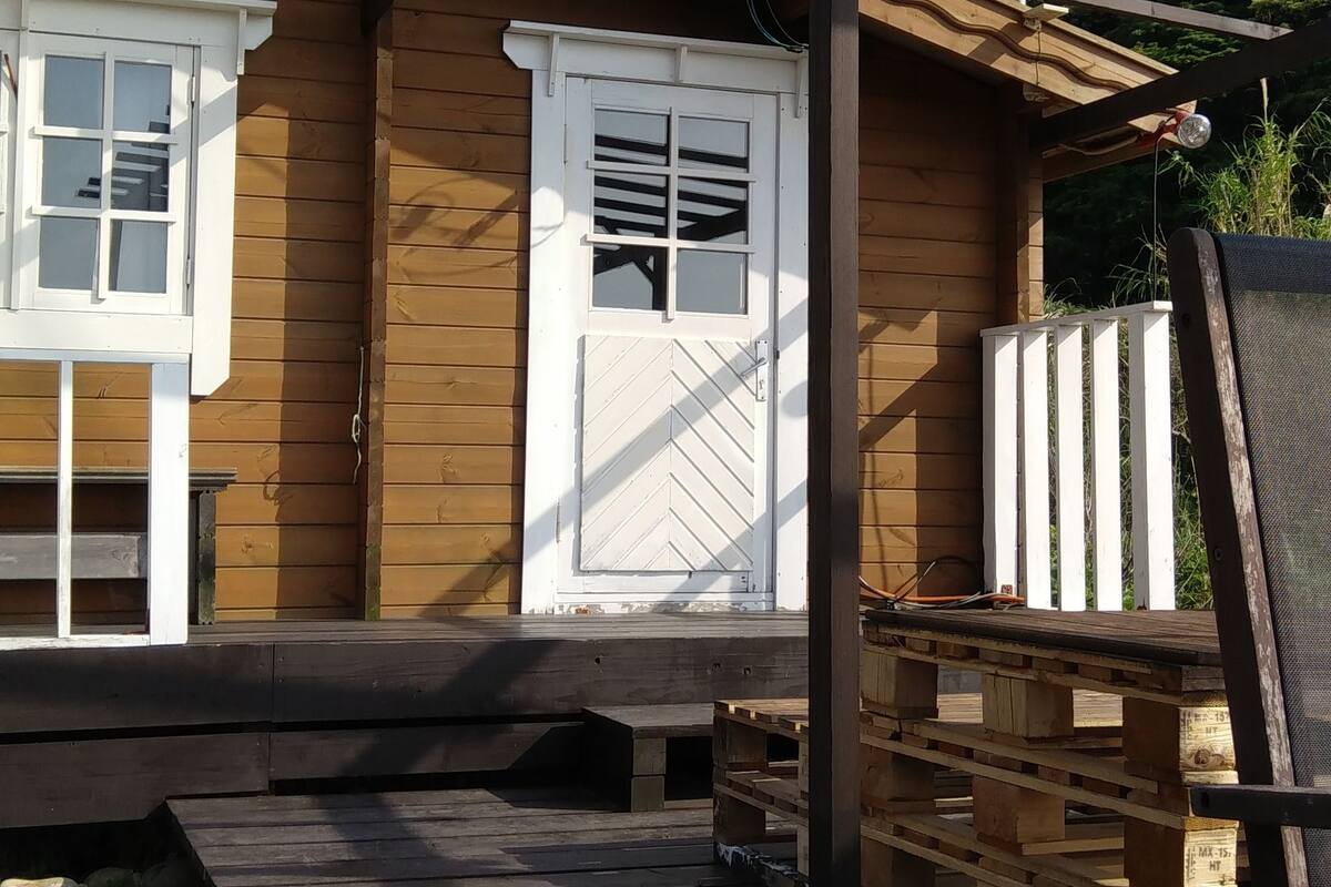 Una cabana de fusta amb una porta i finestres blanques, un balcó de fusta i una estructura de pergola.