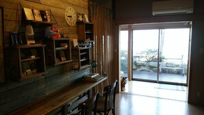 Una habitación con pared de madera, estantes con libros y adornos, un escritorio con máquina de escribir y un ventanal con vistas a rocas y vegetación.