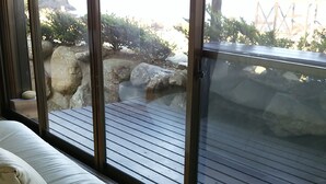 Una habitación con un gran ventanal corredera que da a un espacio exterior con terraza de madera y rocas.