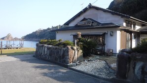 Una casa japonesa tradicional con un muro de piedra, una terraza de madera y vista al mar.