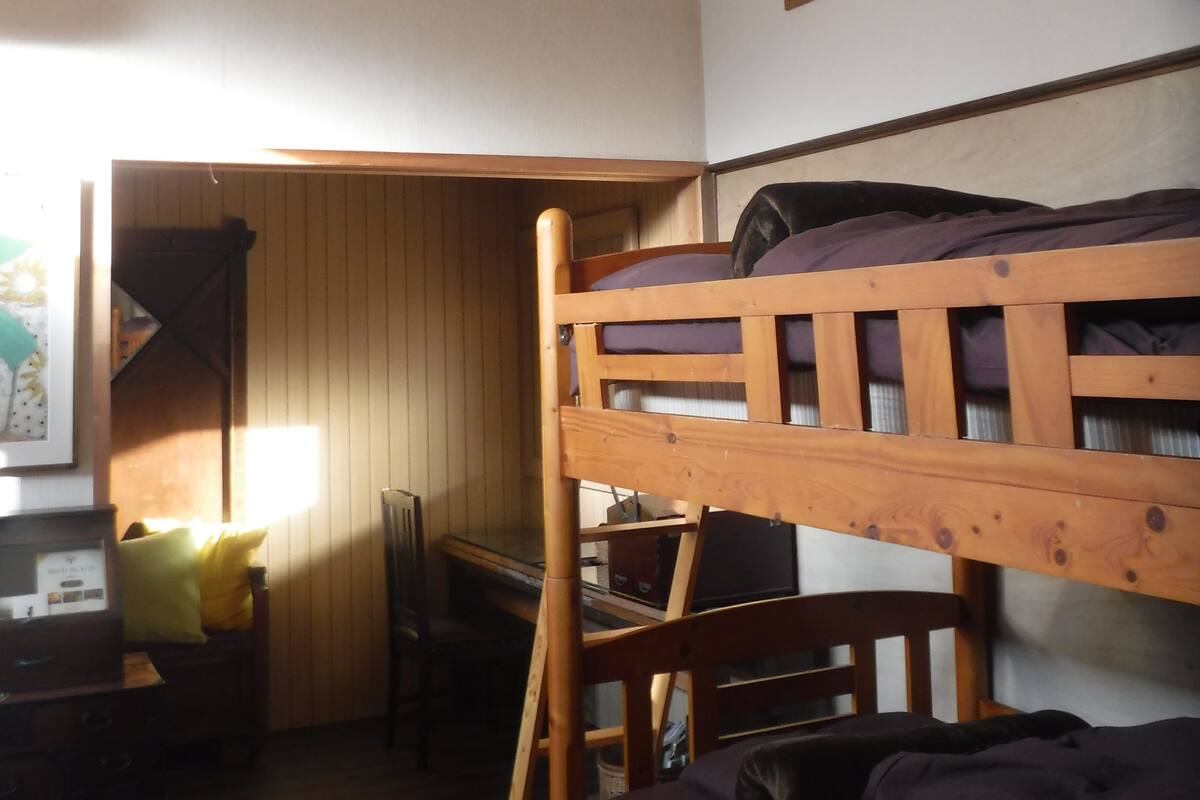 Habitació amb lliteres, escriptori, cadira i un rellotge a la paret.