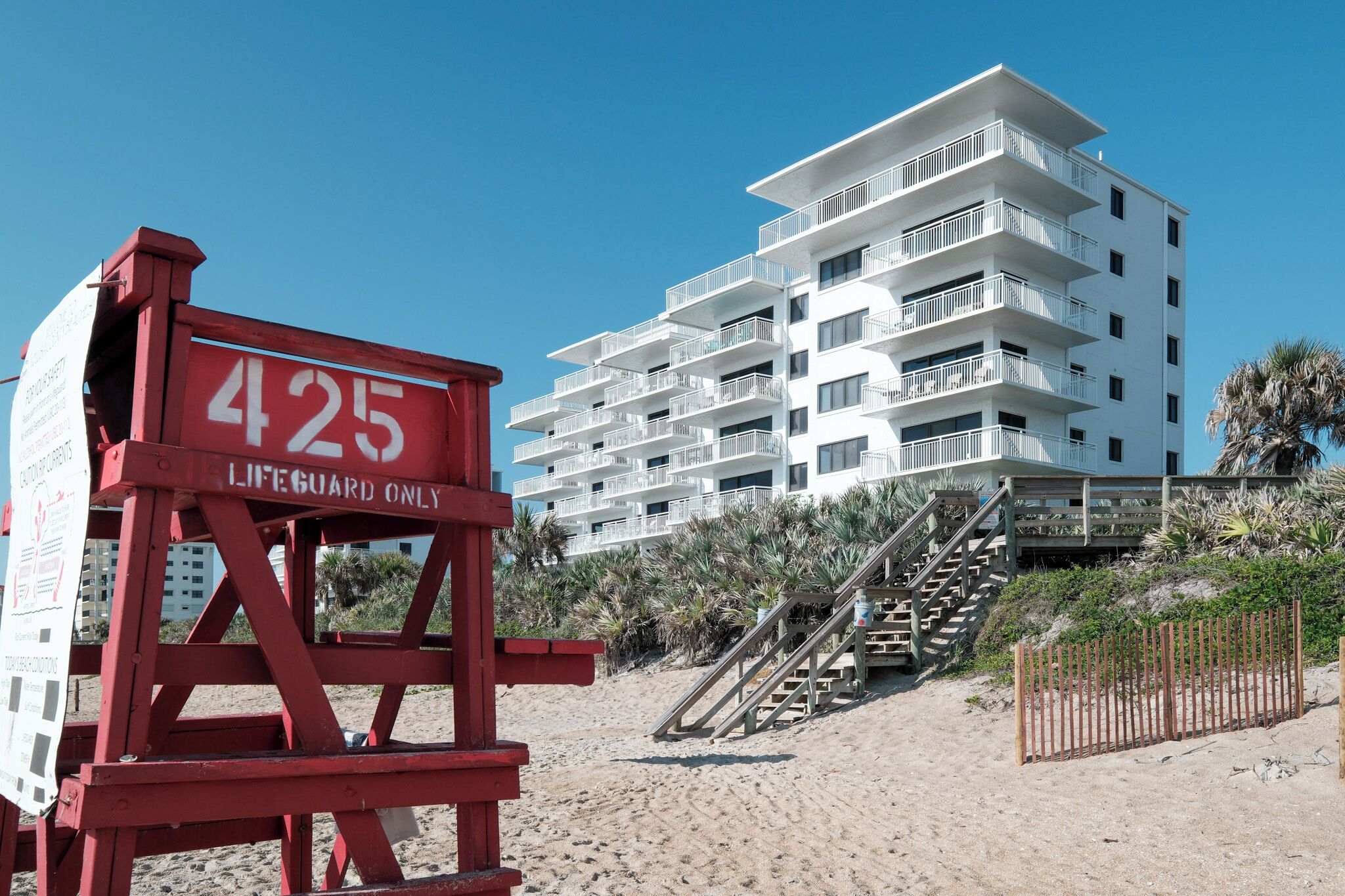 Ein Rettungsschwimmturm mit der Nummer 425 und ein mehrstöckiges Gebäude mit Balkonen im Hintergrund.