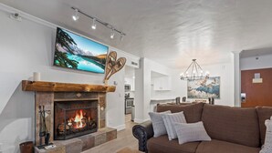 Een woonkamer met een open haard, een bank, een salontafel en een aan de muur bevestigde televisie.