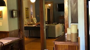 A dining area with a wooden table and chairs, a patterned sofa, and a kitchen in the background. - 3500 SF Original School transformed into an artful,  gorgeous village home, yard (Bar Harbor)