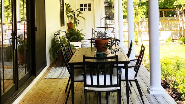 A covered outdoor patio with a wooden table and chairs, potted plants, and a view of the backyard. - 3500 SF Original School transformed into an artful,  gorgeous village home, yard (Bar Harbor)