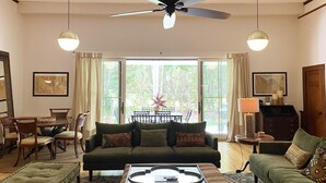 A living room with a sofa, armchair, and coffee table. There is a dining area with chairs and a table. A ceiling fan is visible. - 3500 SF Original School transformed into an artful,  gorgeous village home, yard (Bar Harbor)