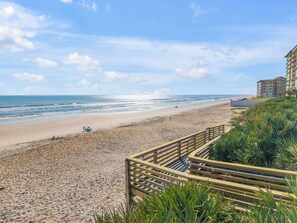 A beach with a wooden boardwalk, ocean view, and a building in the background. - 🌊 Direct Oceanfront 2BR | Large Balcony | Heated Pool & Beach Access 🏖️ (New Smyrna Beach)