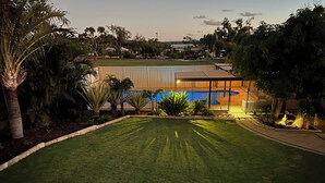 Une pelouse bien entretenue avec une piscine, entourée de palmiers et d’une clôture.