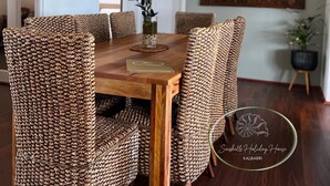 Un coin repas avec une table en bois et des chaises en osier, un vase avec une plante et un tableau encadré au mur.