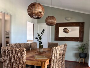 A dining area with a wooden table and woven chairs, a vase with a plant, and a framed picture on the wall.