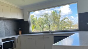 Une cuisine moderne avec des meubles blancs, un four à micro-ondes et une grande fenêtre donnant sur des palmiers.