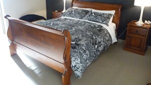 Una cama de madera con una colcha estampada, dos mesitas de noche con lámparas y una pared oscura.