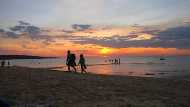 Una playa al atardecer con gente caminando por la orilla.