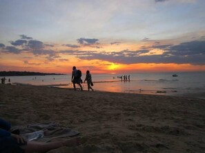 A beach at sunset with people walking along the shore.