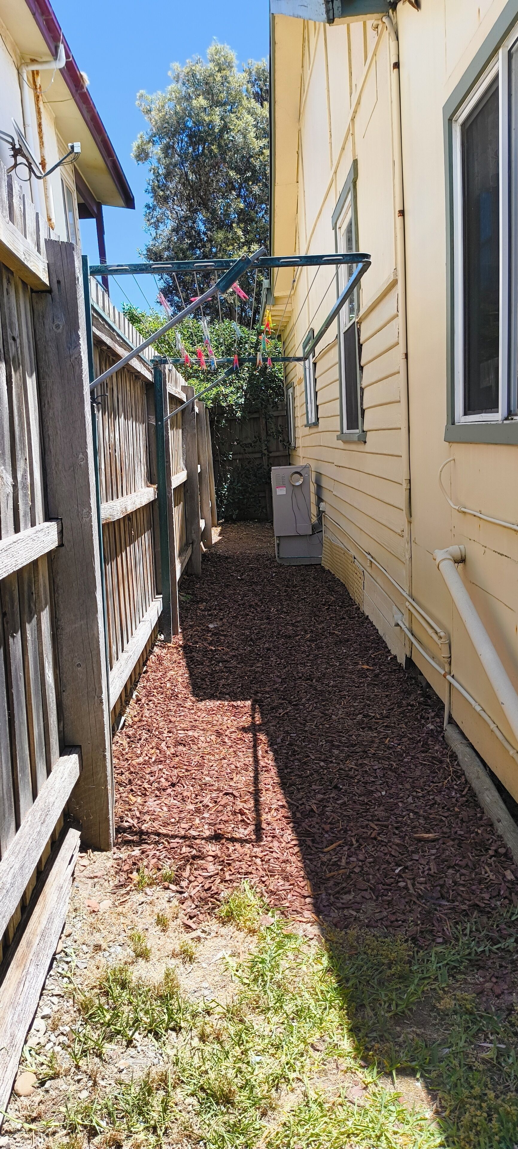 Un étroit sentier extérieur, bordé d’une clôture en bois d’un côté et d’un bâtiment de l’autre.