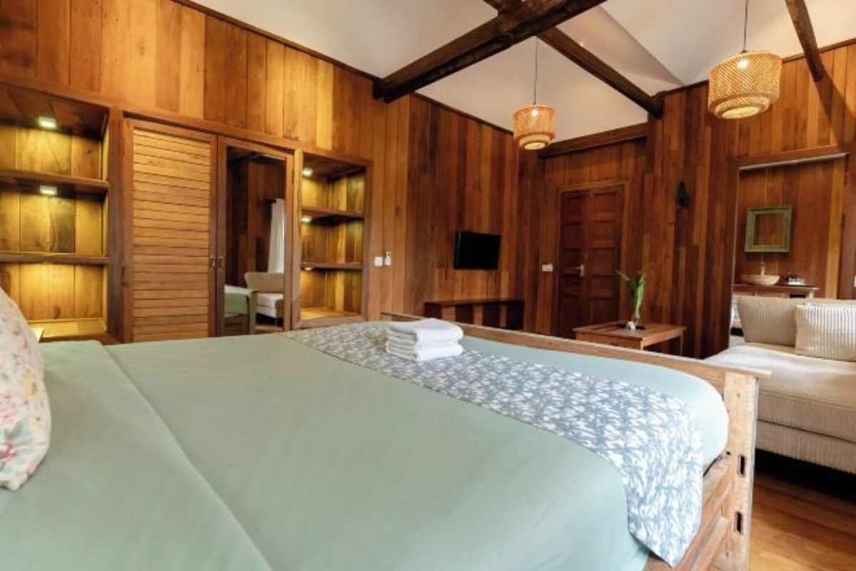A wooden-themed room with a bed, a sofa, and built-in shelves.
