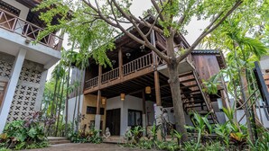 Un bâtiment traditionnel en bois, doté d’un balcon et entouré d’une végétation tropicale luxuriante.