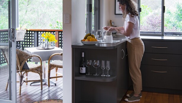 A kitchen with a large window, a dining area with wicker chairs, and a fruit bowl on the counter. - St Clair Cottage Peaceful romantic country getaway  (Margaret River)