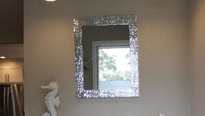 Un intérieur moderne agrémenté d’une console en verre, d’un miroir décoratif et d’un banc blanc à la texture intéressante.