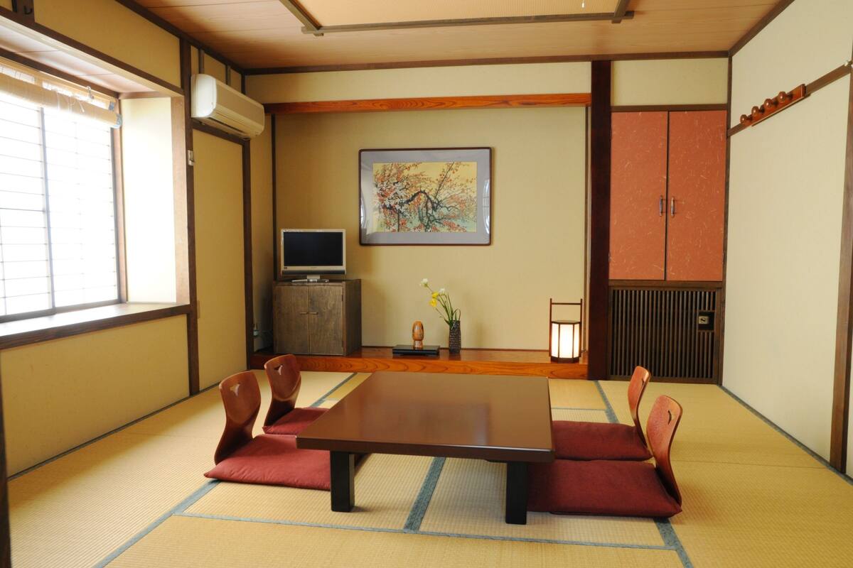 A traditional Japanese room with tatami flooring, a low table, and red cushions.