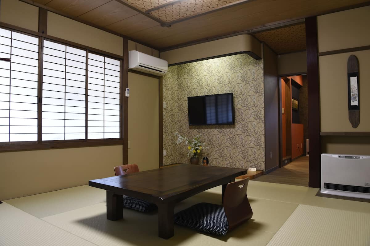 A traditional Japanese room with tatami flooring, a dark wooden table, and a television mounted on the wall.