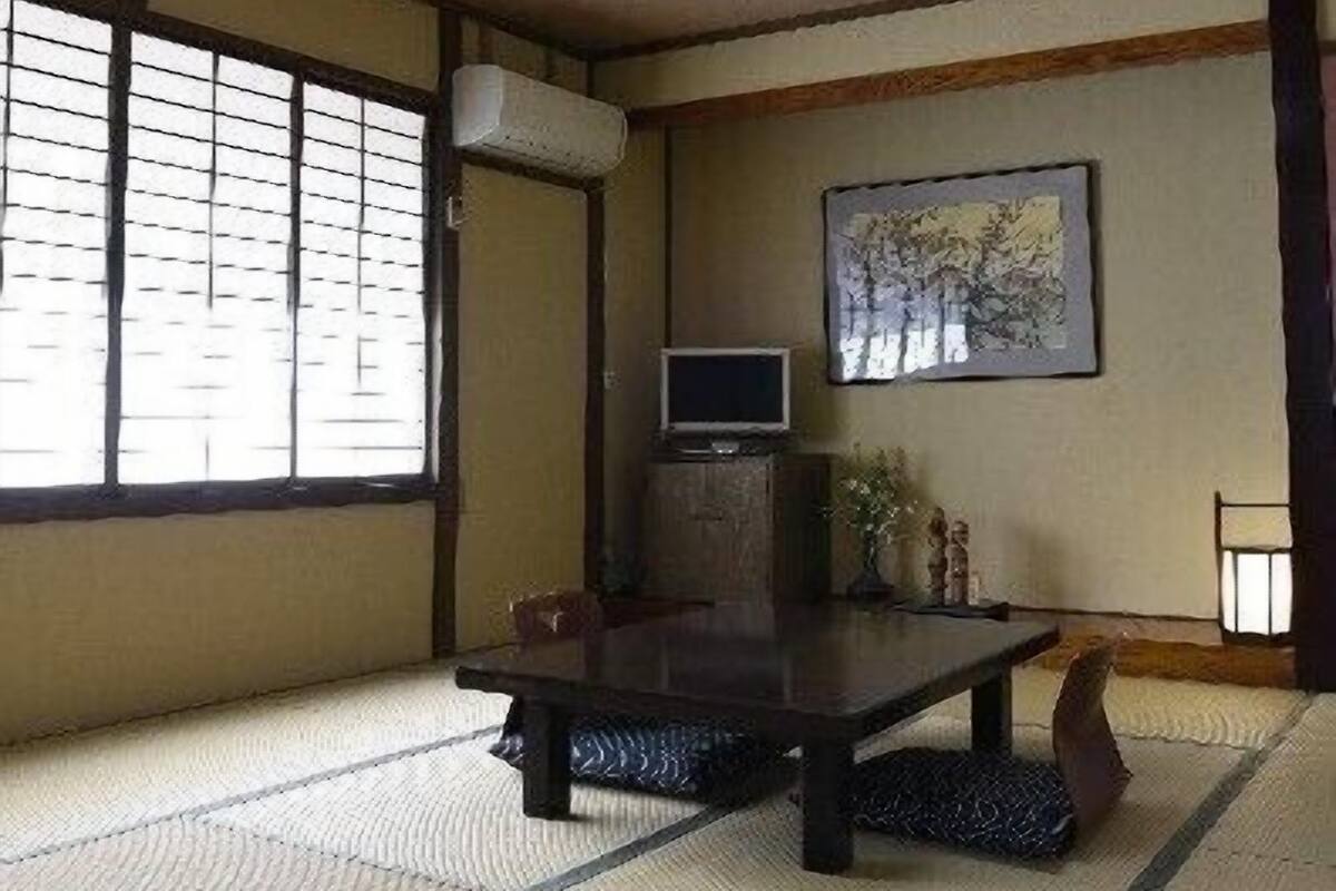 A traditional tatami mat room with a tatami mat table, a television, and a framed artwork on the wall.
