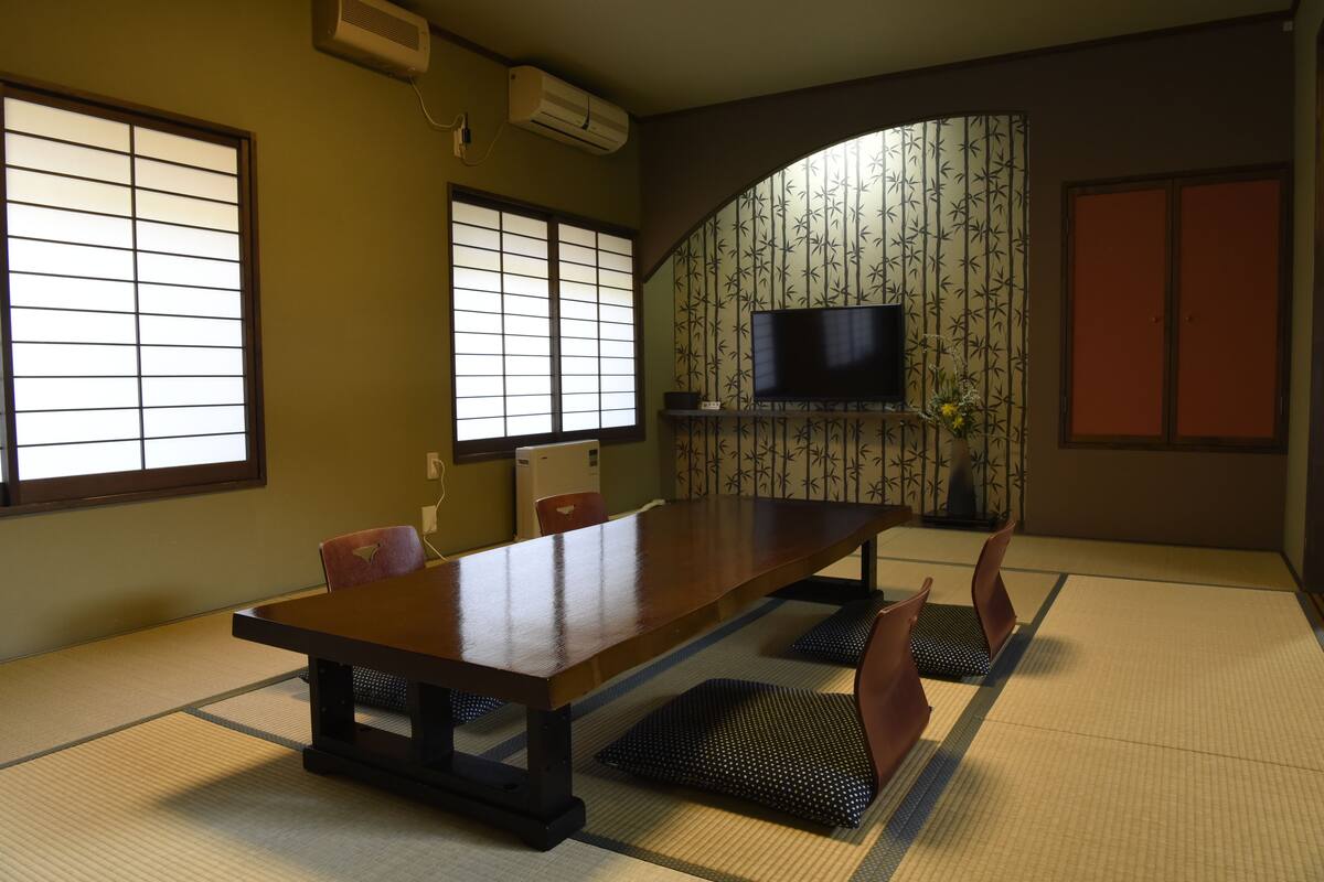 A traditional Japanese room with tatami flooring, a low table, and a television mounted on the wall.