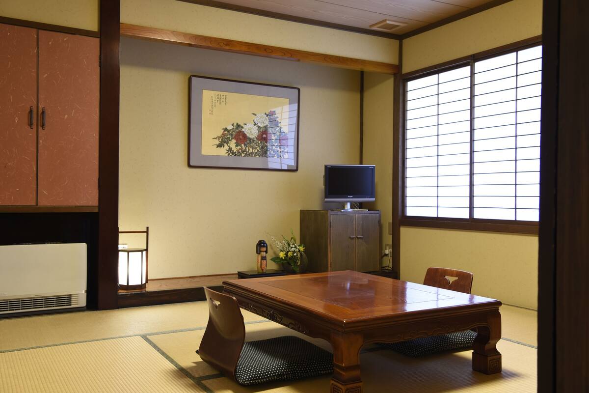 A traditional Japanese room with tatami flooring, a wooden table, a television, and a sliding door.