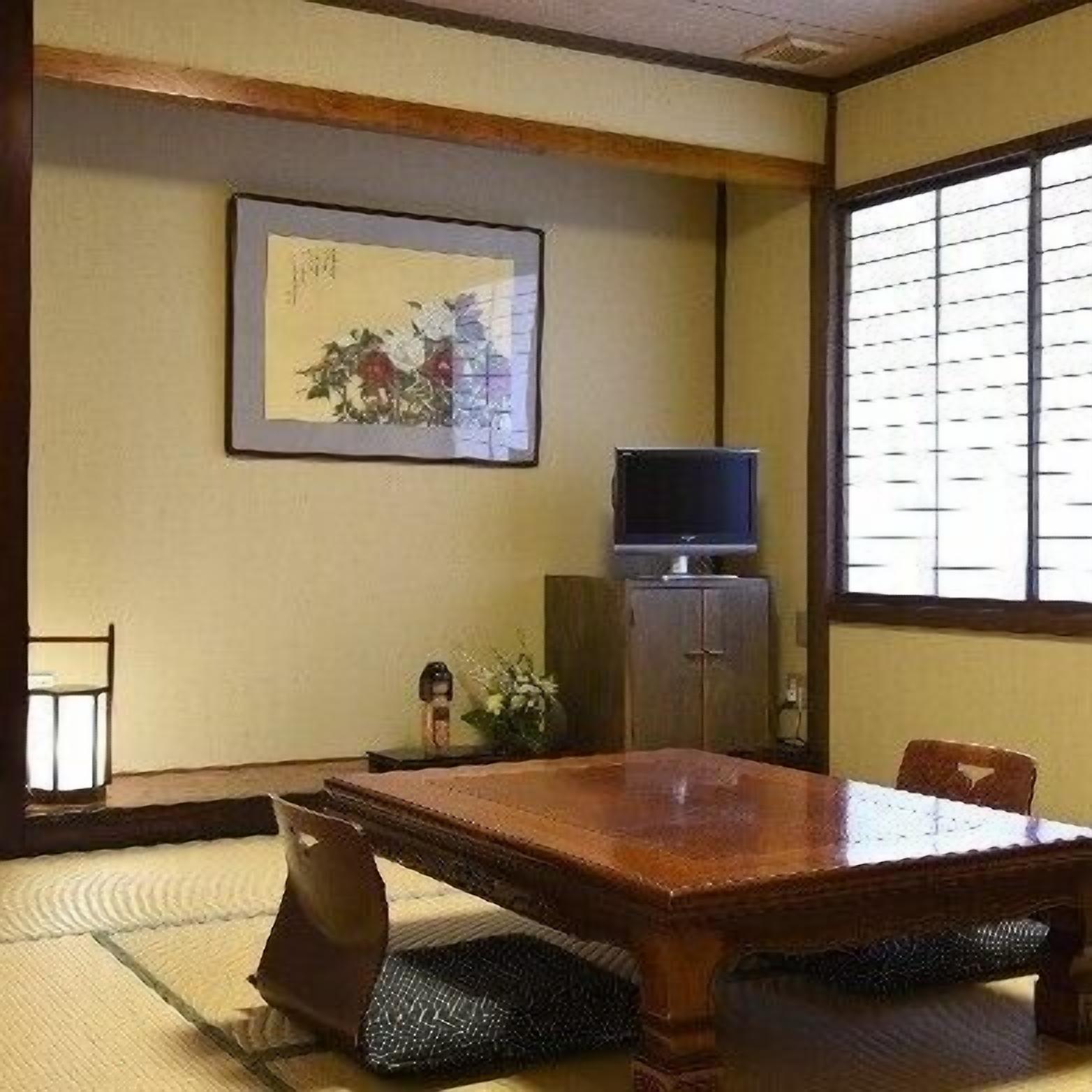 Habitació japonesa tradicional amb sòl de tatami, una taula baixa, un televisor sobre un moble i una obra d'art emmarcada a la paret.