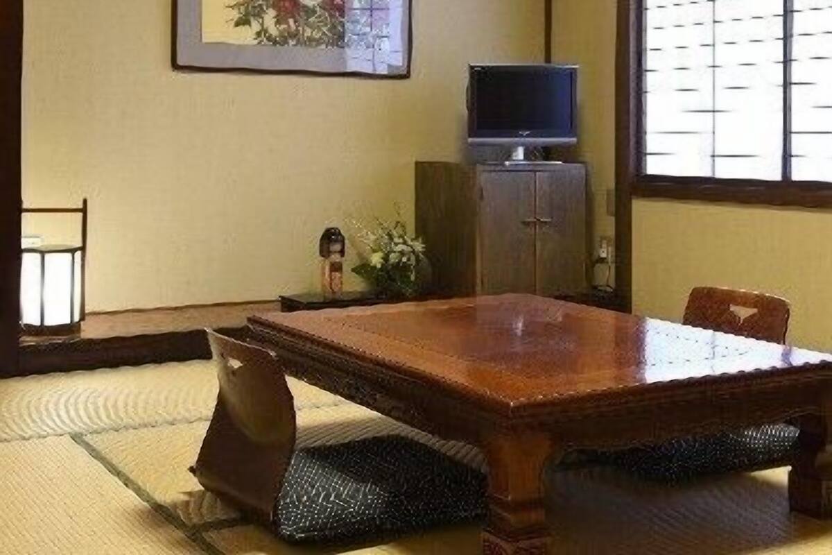 A traditional Japanese-style room with tatami flooring, a low table, a television on a cabinet, and a framed artwork on the wall.