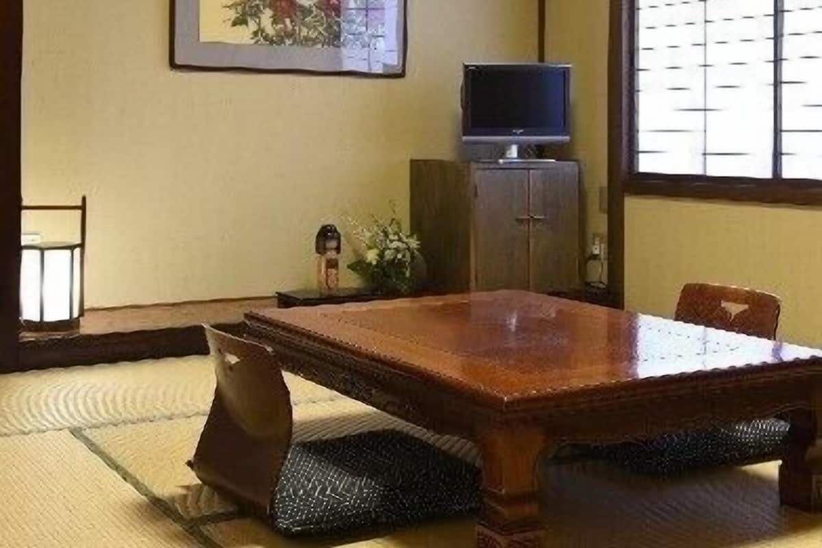 A traditional Japanese-style room with tatami flooring, a low table, a television on a cabinet, and a framed artwork on the wall.