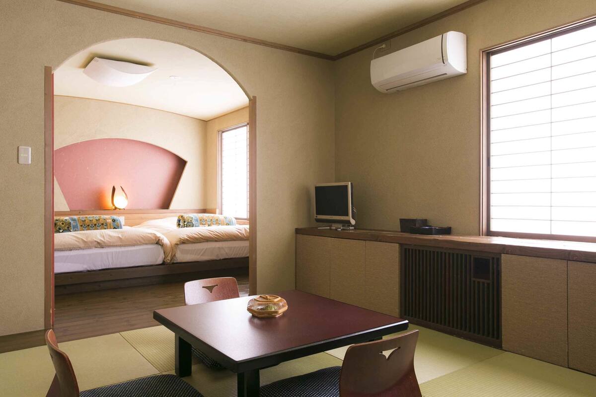 A hotel room with a bed, a desk, a chair, a television, and a window with blinds.