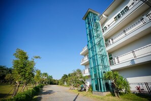 A modern building with a glass tower, multiple balconies, and a pathway leading to the entrance.
