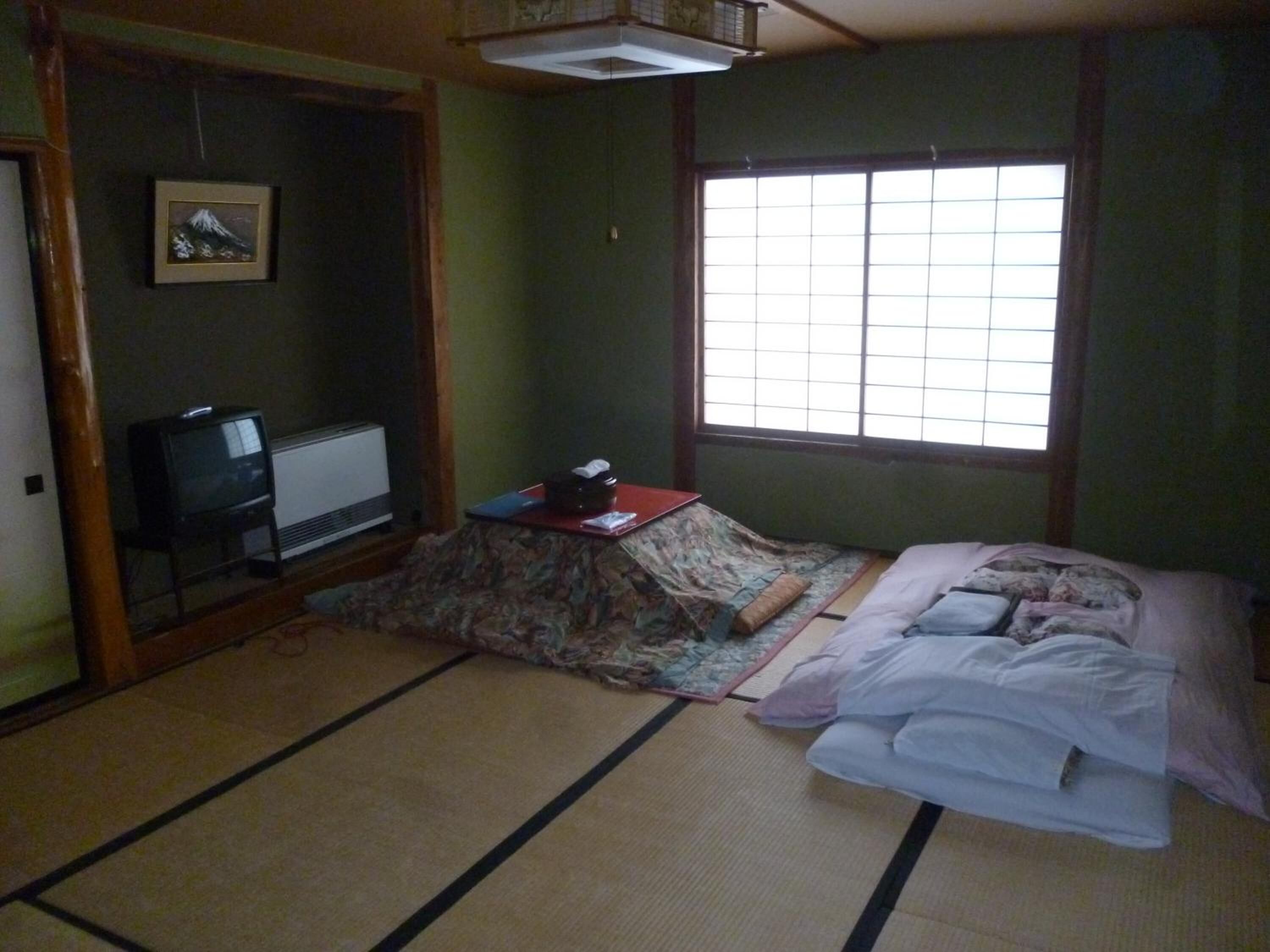 A traditional Japanese room with tatami flooring, a futon bed, a television, and a window with shoji screens.