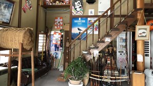 Ein traditionelles japanisches Interieur mit Tatami-Böden, einer Holztreppe und verschiedenen kulturellen Artefakten, darunter eine Uhr, Poster und ein Shoji-Bildschirm.