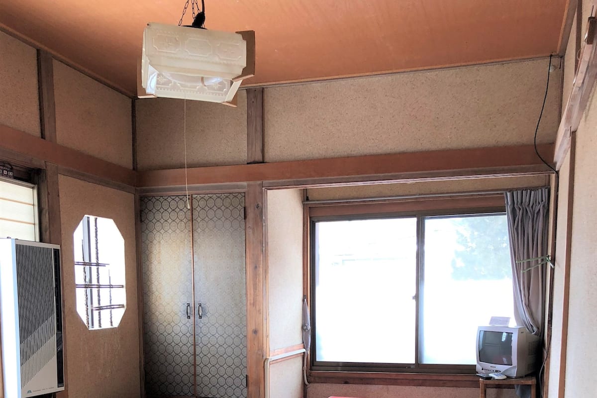 Ein traditioneller japanischer Raum mit Tatami-Matten, einem Futon, einem Heizgerät, einem Fernseher und einem Fenster mit Vorhängen.
