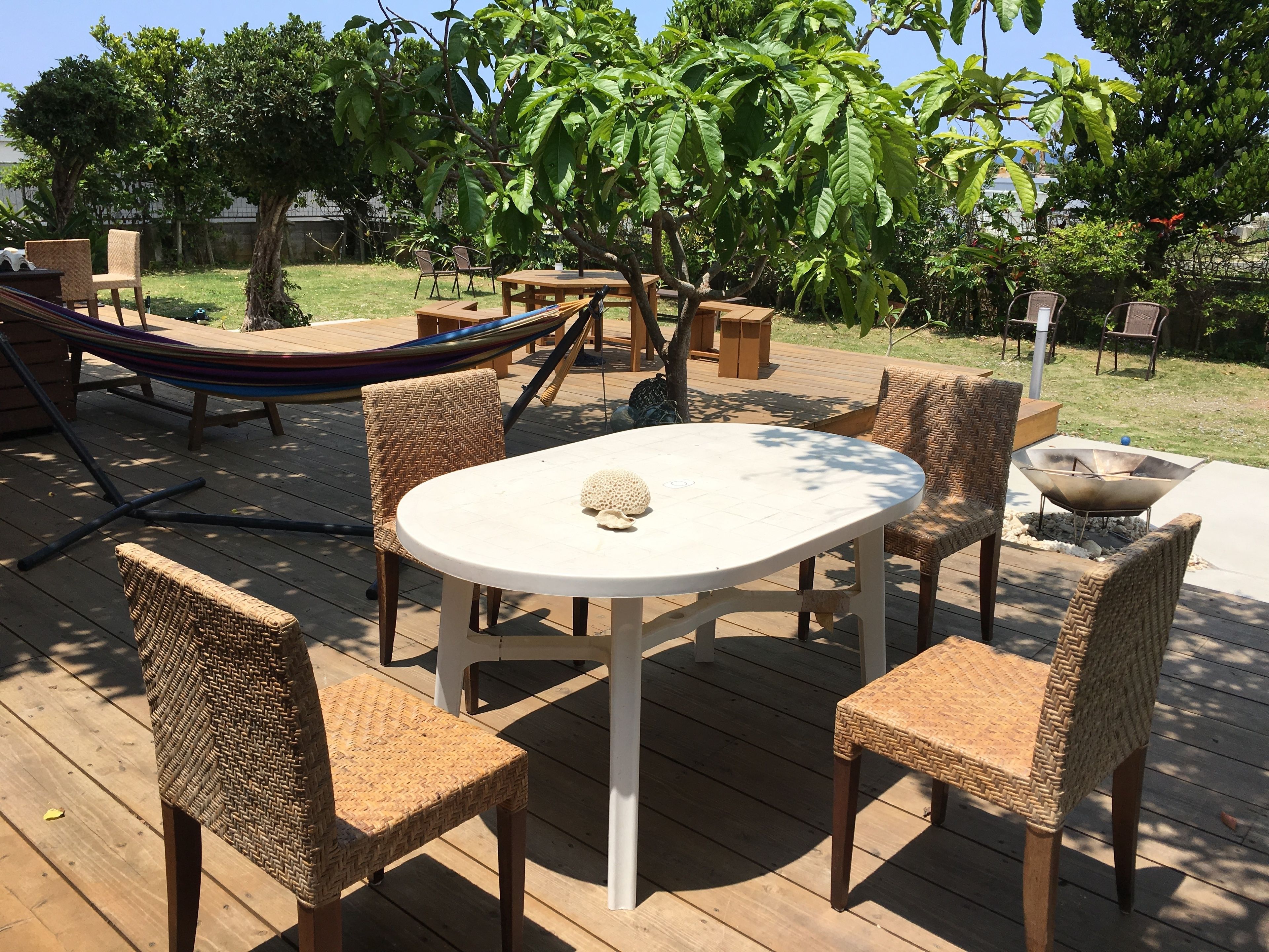 An outdoor patio with a round table and four wicker chairs, surrounded by wooden deck and greenery.