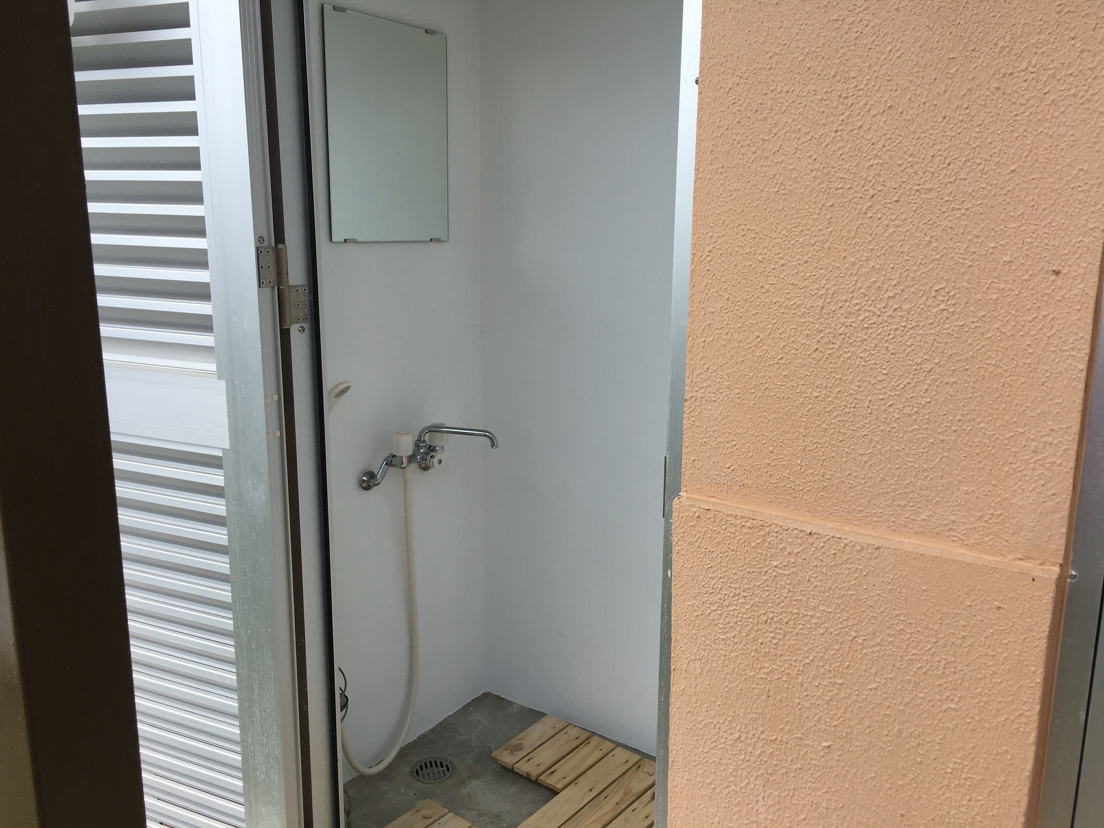 A small, enclosed shower area with a showerhead, a wall-mounted mirror, and a wooden floor.