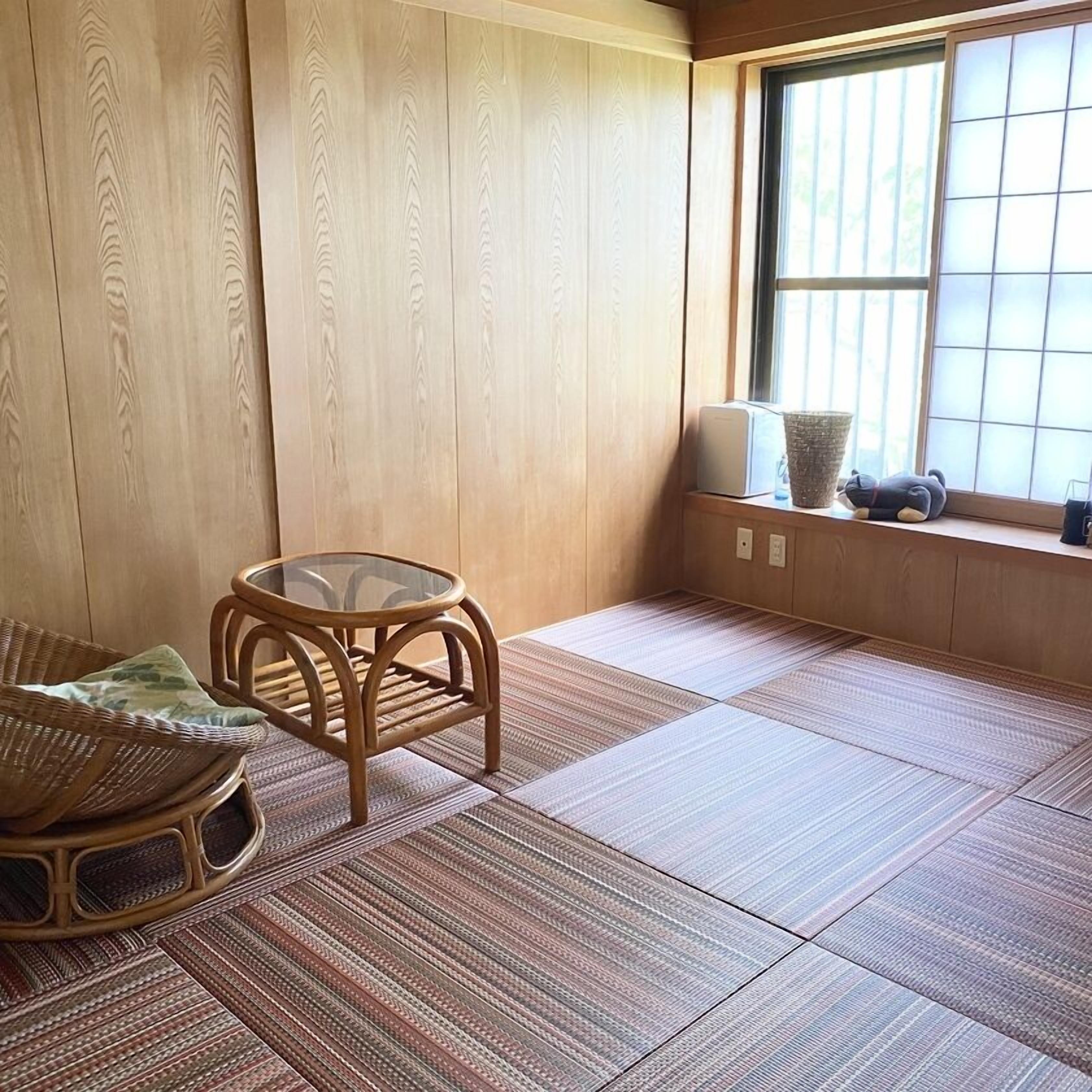 A tatami mat room with a low table, a woven chair, and a window with a view.