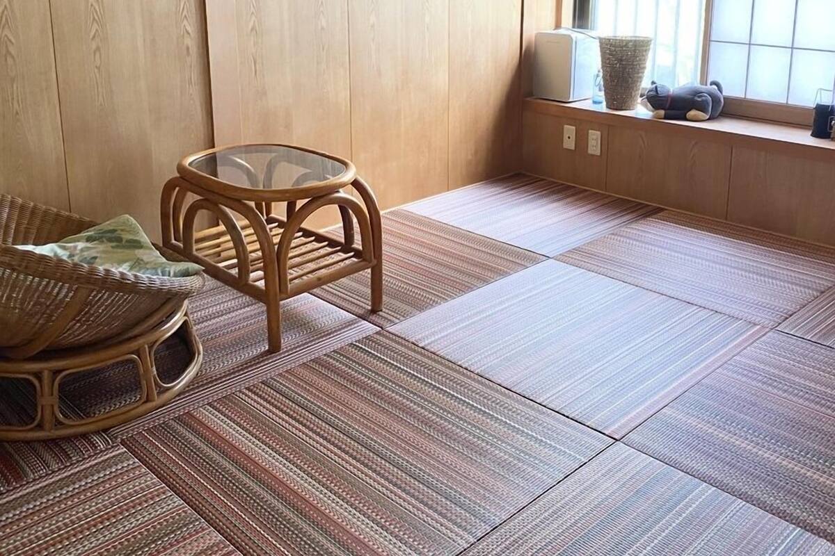A tatami mat room with a low table, a woven chair, and a window with a view.