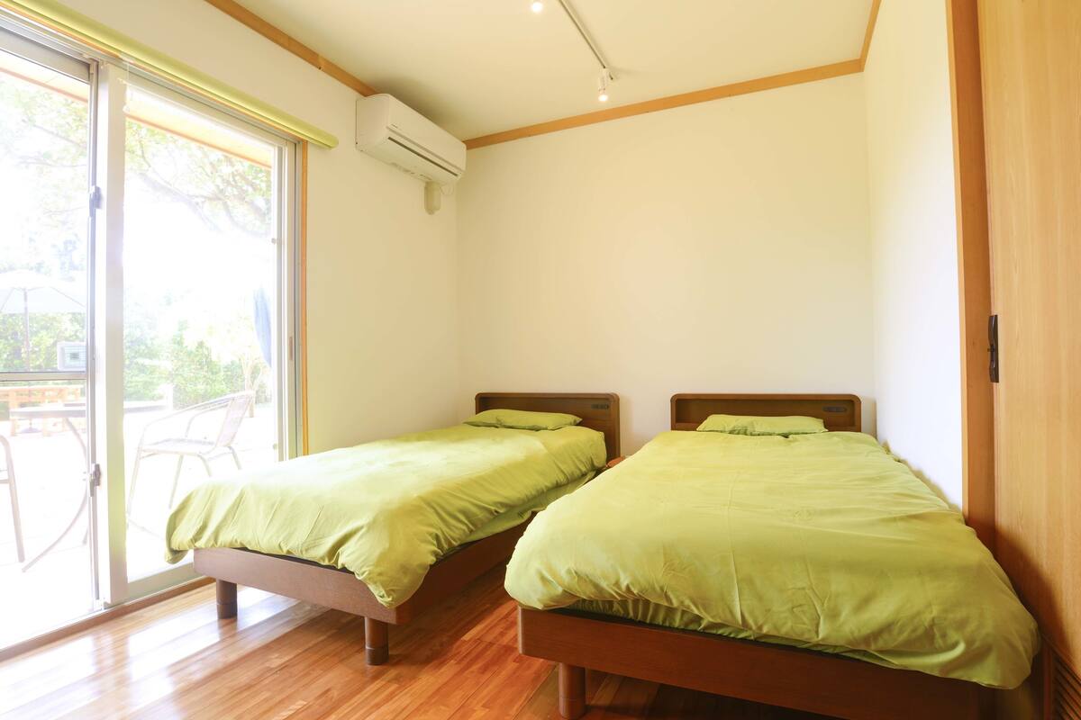 A room with two wooden beds, a sliding glass door to the outside, and an air conditioning unit on the wall.