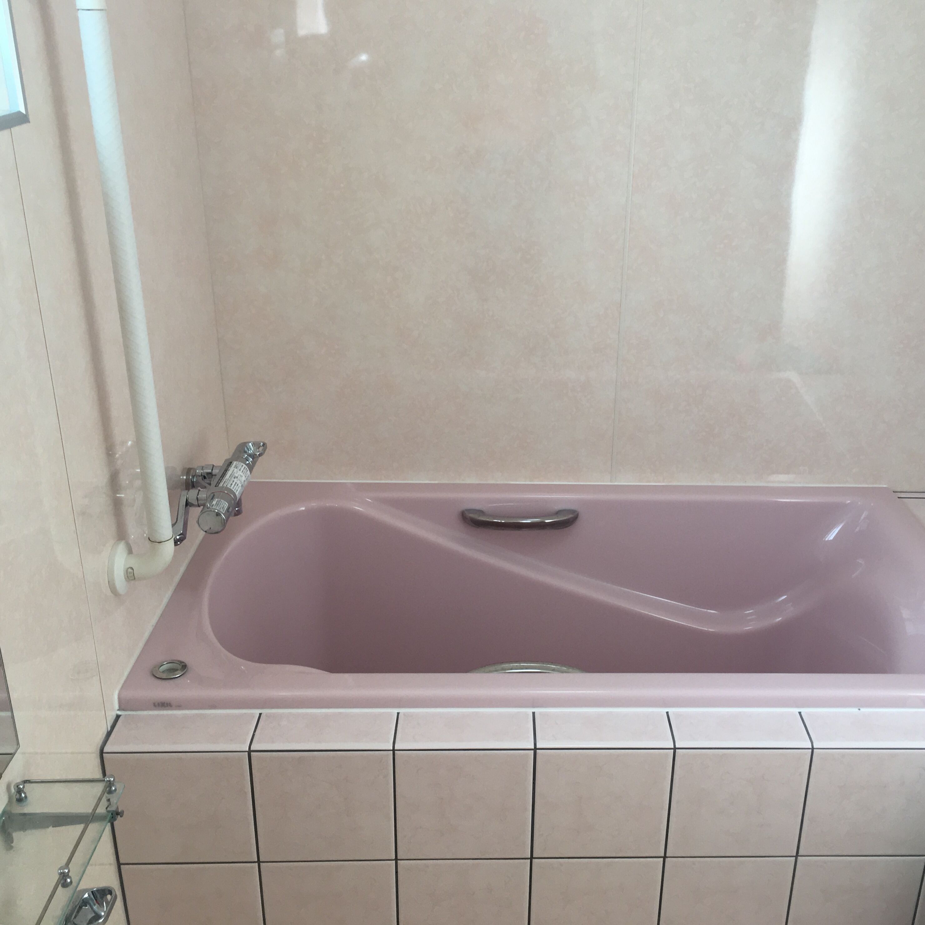 Une salle de bain avec une baignoire rose, des murs recouverts de carreaux blancs et une cabine de douche en verre.