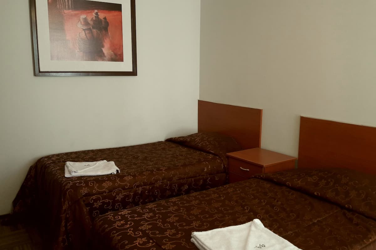 Ein Hotelzimmer mit zwei Betten, einem gerahmten Bild an der Wand und einem kleinen Nachttisch aus Holz.