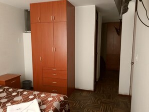 Un dormitorio con una cama, un armario, una mesita pequeña y un cubo de basura.