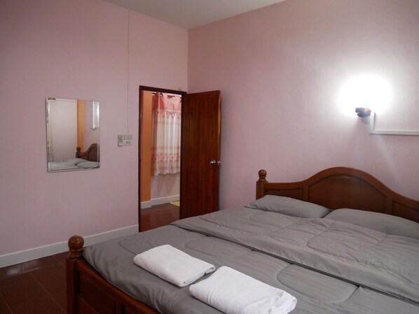 Un dormitorio con una cama de madera, un espejo y una puerta que da a un baño.